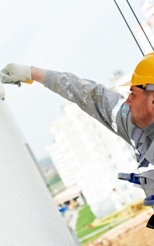 Building facade painting. builder worker painter covering outside wall with paint by roller